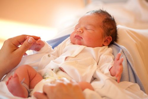 A baby boy with his eyes closed and hand being held.