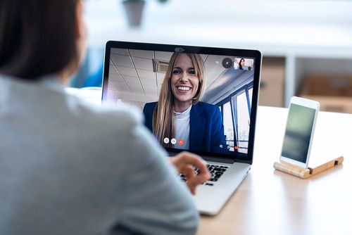 Person having a video call on a laptop with a smiling woman in a blue jacket.